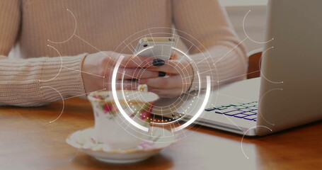 Man wearing pink knit sweater scrolling smartphone at table, with floral teacup and digital overlay