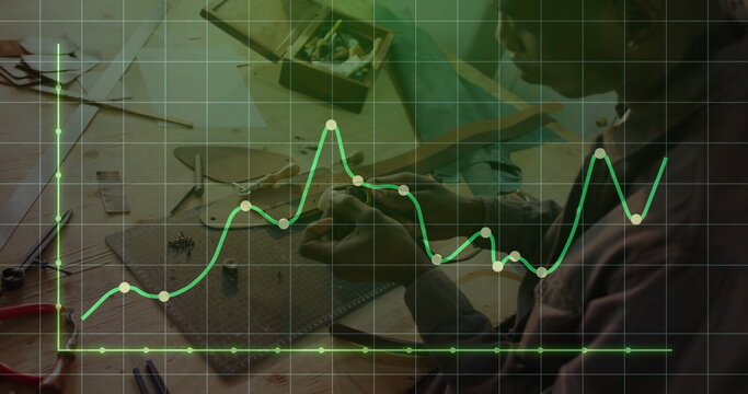 African American craftsman assembling components at bench, with cutting mat and line graph overlay