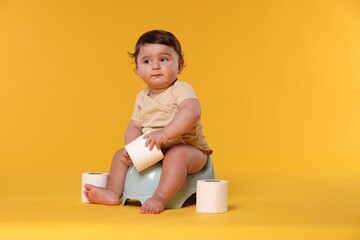 Cute little baby sitting on potty and rolls of toilet paper against orange background