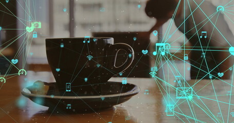Displaying dark ceramic coffee cup nesting on saucer over table at cafe, with teal network icons
