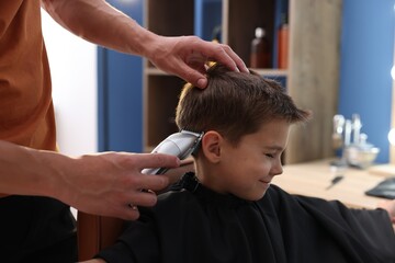 Professional barber working with little boy in barbershop, closeup