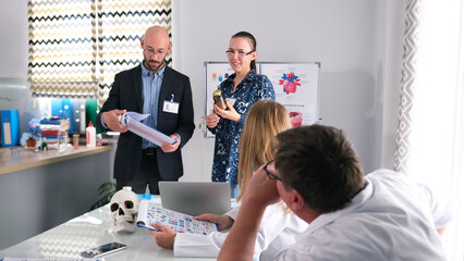 A personable man and his female assistant present a new drug to a group of doctors at a briefing at...