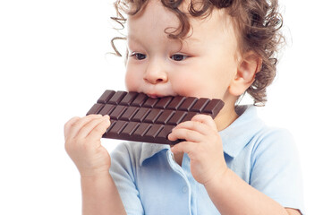 Cute curly haired toddler eating delicious chocolate with a happy smile