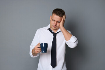 Man with cup of drink suffering from hangover on grey background
