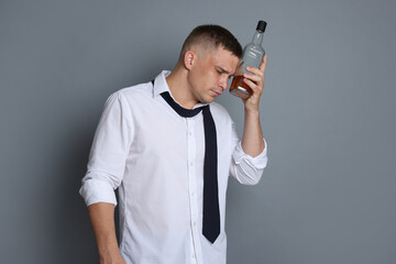 Man with bottle of whiskey suffering from hangover on grey background
