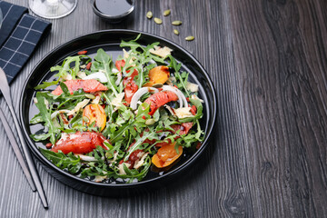 Tasty salad with arugula, cheese, grapefruit, vegetable and balsamic sauce on dark wooden table, closeup. Space for text