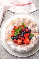 Tasty Bundt cake with powdered sugar and berries on grey textured table, top view