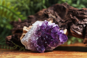 Aura. Beautiful amethyst and driftwood on wooden surface against blurred green background