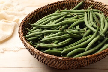 Fresh pea pods in wicker basket on light wooden table, closeup