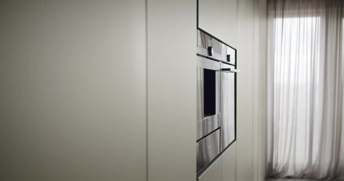 A sleek, modern kitchen detail featuring a reflective glass cabinet beside a softly draped white curtain. Minimalist interior design captured in natural light. Modern Kitchen