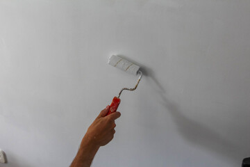 Professional paint brush with red handle held in hand during precise interior wall painting renovation work