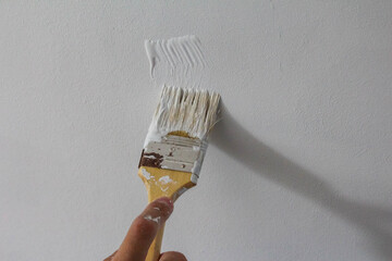 Paint brush with wooden handle applying white paint to wall surface during professional interior...