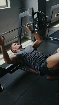 Athlete engaging in a strength training session, lifting a barbell on a bench press at a gym. The image portrays fitness, dedication, strength, and health. Man Working Out With Barbell In Gym Vertical