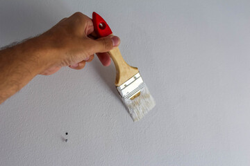 Human hand demonstrating proper paint brush holding technique with red handle against white surface...
