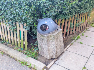 Modern cylindrical concrete waste bin positioned on paved walkway near wooden fence in residential...