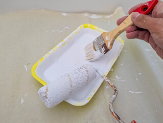 Painter's hand holding red-handled brush while carefully taping around electrical outlet during wall preparation process