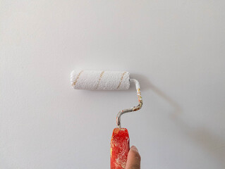 White paint roller with red handle positioned for wall painting during home renovation interior project