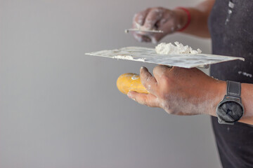 Hands of a construction worker applying plaster on trowel with putty knife