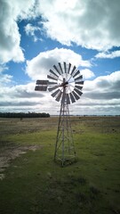 Solitary windmill on a vast green field under a blue sky.