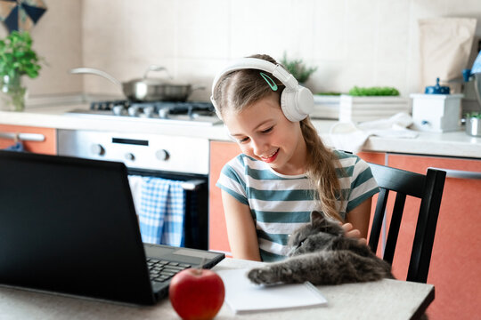 Happy school girl in headphones using laptop with cat at home. Online education for kids, homeschooling, gamified distance learning in cozy studying space. Digital childhood, technology lifestyle