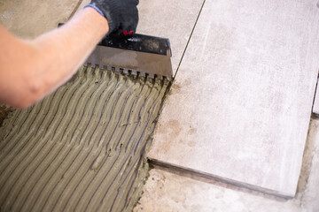 Close-up of notched trowel spreading tile adhesive evenly before laying ceramic floor tiles