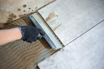 Applying tile adhesive with a notched trowel to the floor before laying large-format tiles