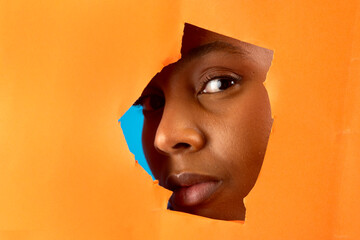 Curious model peeking through torn orange paper with blue background