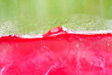 Close-up of a refreshing red drink with ice cubes, condensation droplets on the glass, and a soft...
