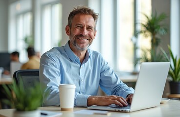 Smiling man in light blue shirt works on laptop in coworking space. Drinks coffee from takeaway cup. Mature, experienced pro focused on business task. Successful entrepreneur, positive vibe.