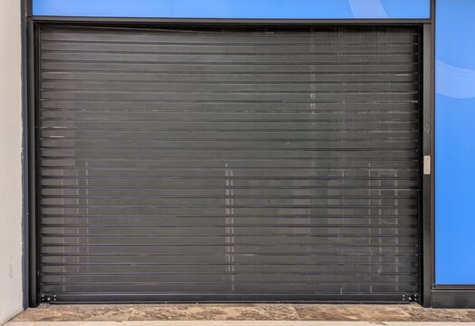 Fachada de una tienda con puerta cerrada por cortina plegable de metal en centro comercial	