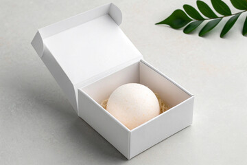 White bath bomb in an open gift box with a leaf