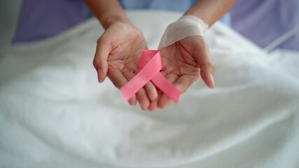 Patient woman hands holding pink ribbon in hospital for rising health awareness on February 4 world cancer day, breast cancer awareness and supporting people life concept.