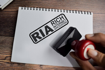 Red Handle Rubber Stamper and RIA - Rich Internet application text above book isolated on wooden background