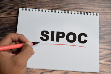 Concept of Sipoc - Suppliers inputs process outputs and customers write on book isolated on Wooden Table.