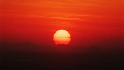 Fototapeta premium Vibrant red sunset above a silhouetted landscape with clear sky, displaying natural beauty and warm light.