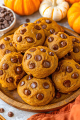 Homemade pumpkin chocolate chip cookies stacked high on a wooden plate. Fall baking.