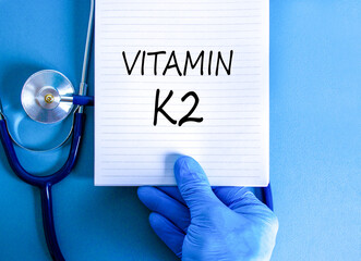 Vitamin K2 phylloquinone symbol. Concept words Vitamin K2 on beautiful note. Doctor's hand in blue...