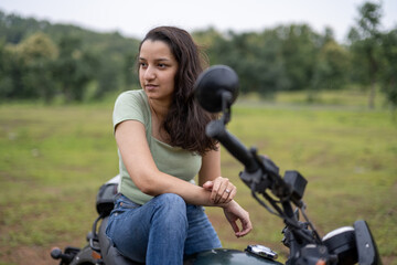 Fototapeta premium Strong independent Indian woman biker: beautiful girl, stylish rider, motorcycle adventure, elegant jacket, confident posture, powerful machine, free spirit, road journey, fearless attitude.