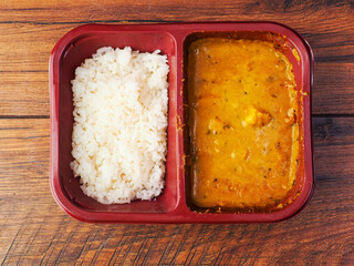 Indian fast food meal with white rice and chicken curry. Popular dish. Tasty ingredients and spices. Product for heating in microwave. Quick and delicious orient style food. Wooden table background.