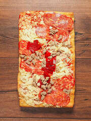 Meat feast pizza with different kind of salami and ham in rectangular shape on wooden background. Popular Italian dish with dough base, tomato sauce, cheese and other ingredients and spices.