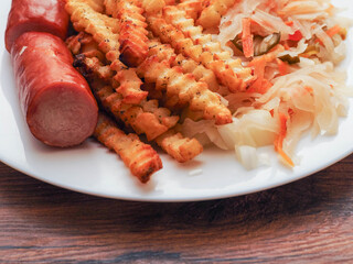 A plate of food with a hot dog and French fries on it and sauerkraut salad. The plate is on a...