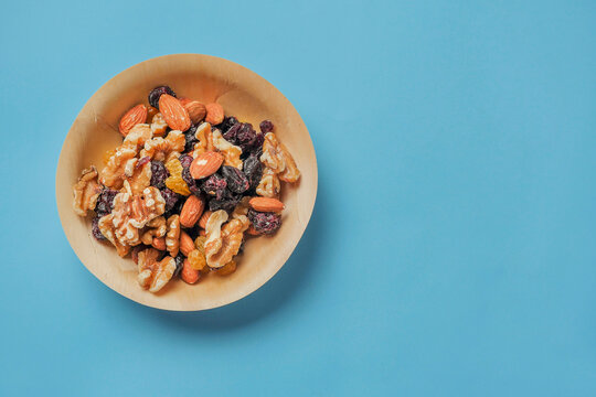 A bowl of nuts and dried fruit on a blue medical background. The bowl is made of wood and the food is colorful. Healthy diet add on. Eat natural food concept.
