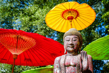 Serene Buddha statue under colorful parasols in a tranquil garden setting during a sunny afternoon