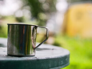 Stainless cup for tea or coffee is on a plastic table, Rural country side background. Selective focus.