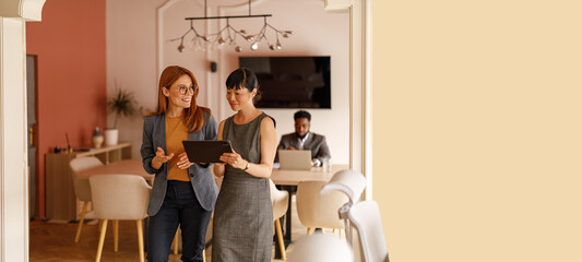 Female professionals using digital tablet to review reports and collaborate on problem solving and...