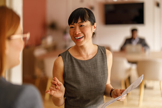 Happy female manager with documents sharing new ideas about project to her partner in modern workplace