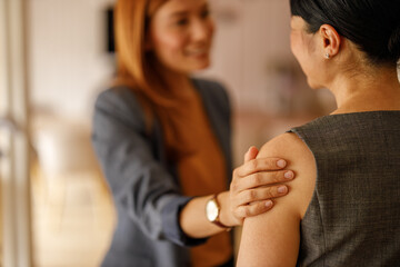 Businesswoman talking to colleague with hand on shoulder in supportive gesture at corporate...
