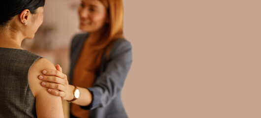 Businesswoman supporting female colleague with hand on shoulder during conversation in corporate office