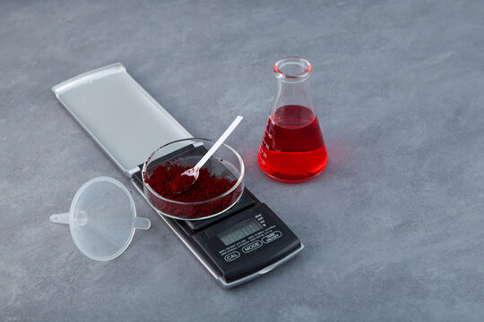 Red azo dye azorubine or carmoisine dissolved in water in glass lab flask. Food dye powder in Petri dish on digital scale. Food additive E122 also know as Food Red 3 or Azorubin S. Colorant
