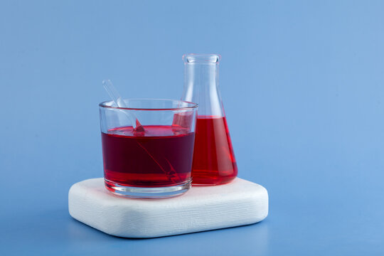 Powder of Azorubine or Carmoisine dissolved in water in various concentrations. Red liquid in glass cup and lab flask. E122, Controversial food dye can be found in jams, syrups, drinks and juices